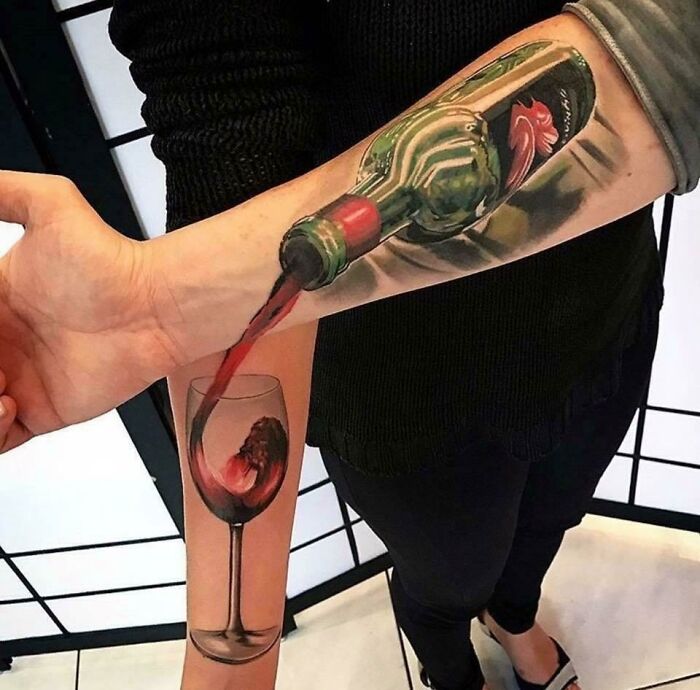Realistic tattoo of a wine bottle pouring into a glass on forearm, showcasing quality tattoo with humorous design flaw.