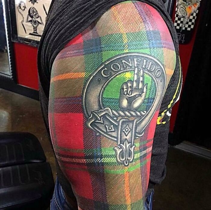 Plaid tattoo design with "Confido" text and a hand symbol, highlighting quality but poor design choice.