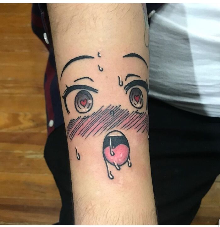 Anime-style tattoo design on forearm with expressive eyes and open mouth, blushing cheeks and sweat droplets.