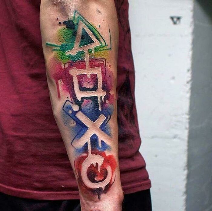 Colorful forearm tattoo with geometric shapes and splatter art against a maroon shirt background.