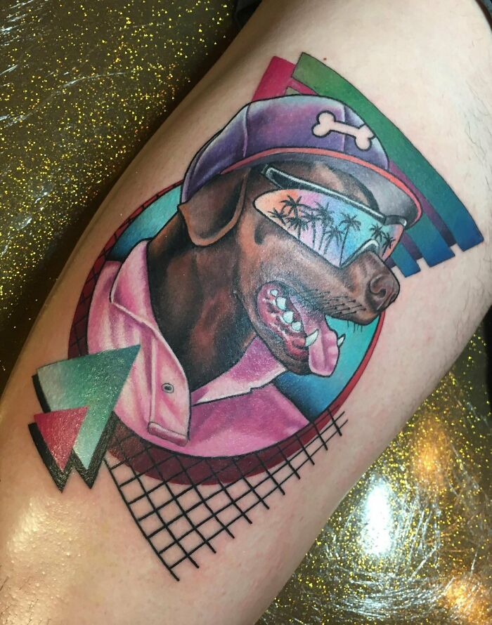 Quality tattoo of a dog in a hat and sunglasses with geometric design elements on a person's skin.
