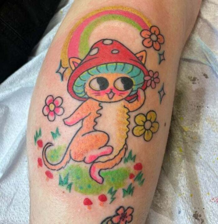 Trippy tattoo of a cat with a mushroom hat and flowers on an arm.