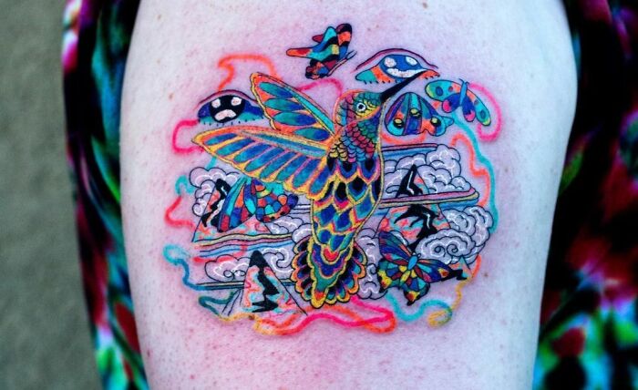 Colorful trippy tattoo of a bird with butterflies on a shoulder, showcasing vibrant and intricate design elements.