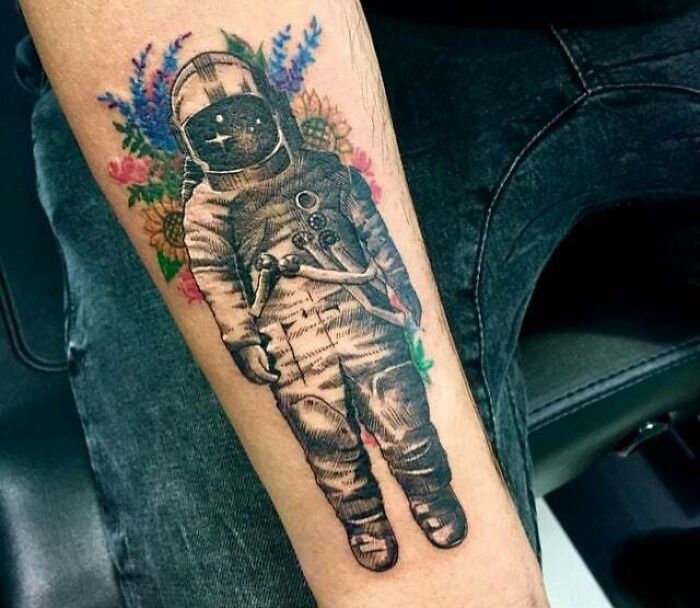 Astronaut with floral design tattoo on arm, showcasing a trippy tattoo idea.