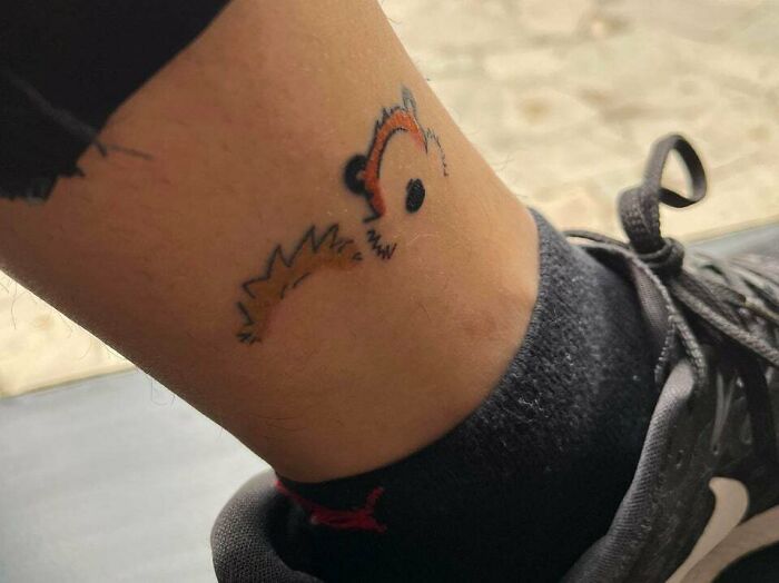 Minimal tattoo of a fox outline on an ankle, next to a black sneaker, showcasing simple yet expressive design.