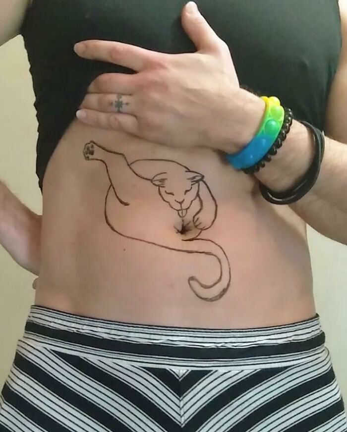 Person shows a cat tattoo on their abdomen, with colorful bracelets.