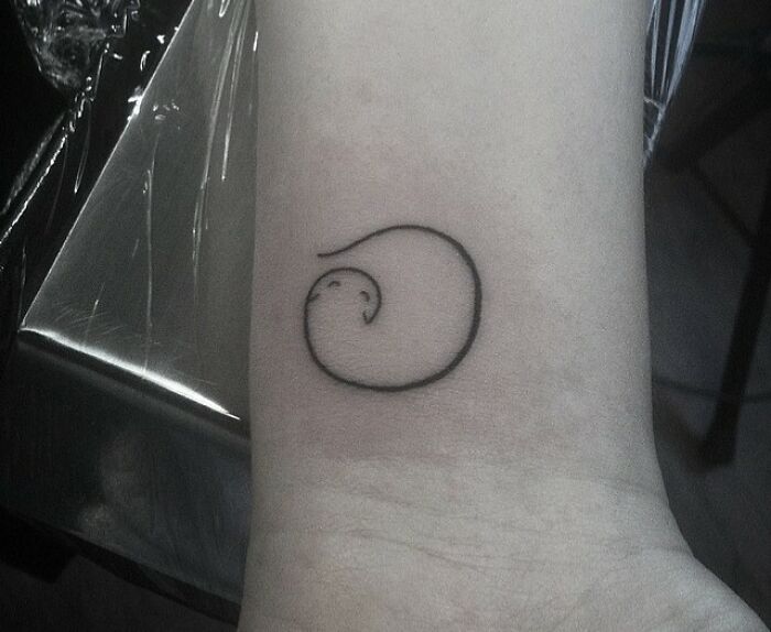 Minimal tattoo design of a small, abstract swirl on a wrist.