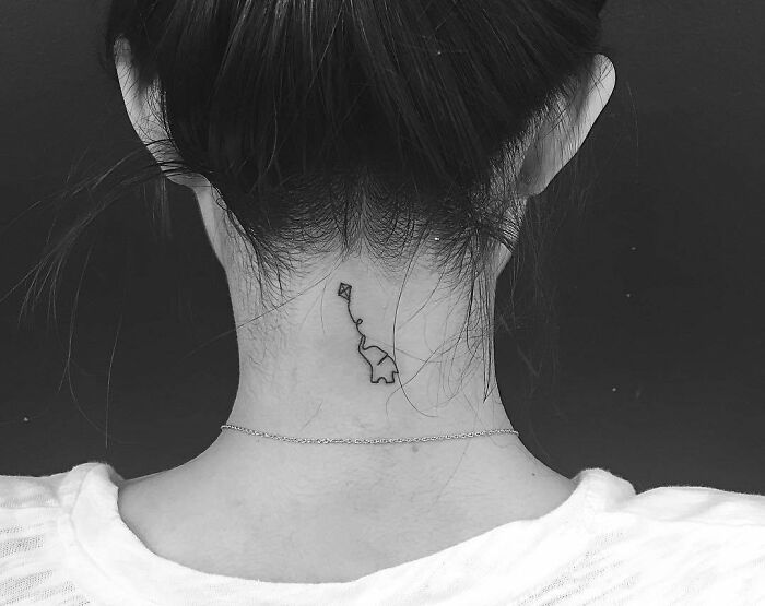 Minimal tattoo design of a simple line art on the back of a woman's neck, seen from behind in black and white.