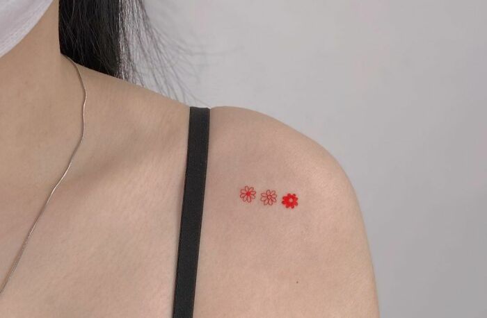 Minimal tattoo of three red flowers on a woman's shoulder.