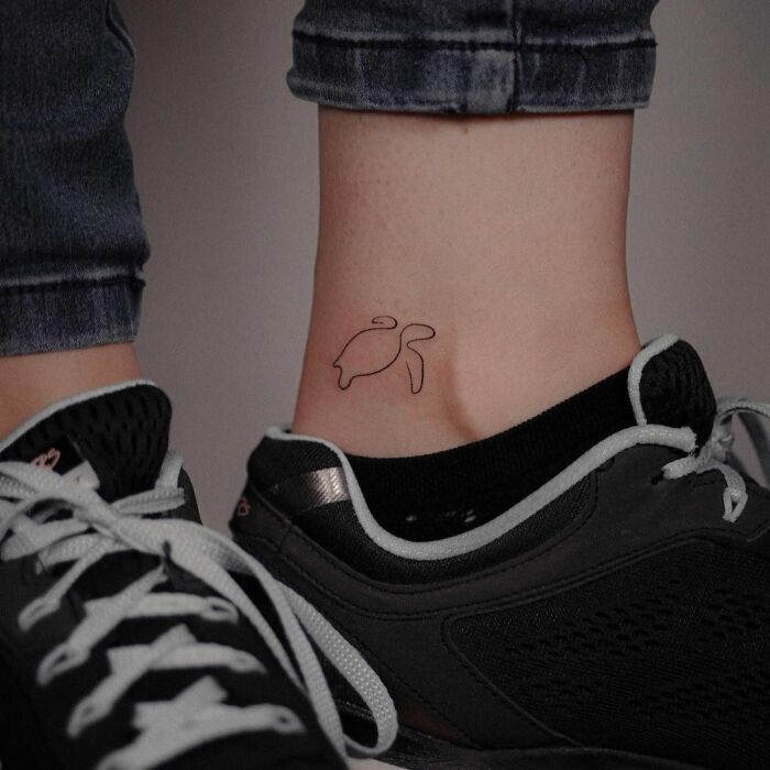 Minimal tattoo design of a simple turtle on an ankle, next to black sneakers and blue jeans.