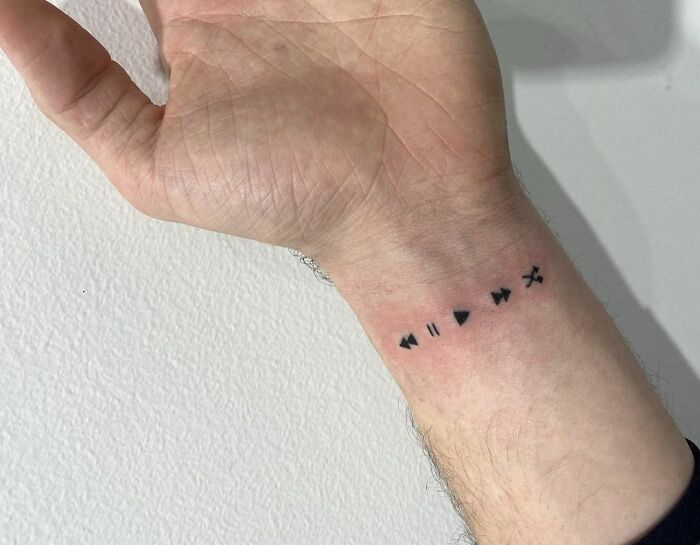 Minimal tattoo design featuring music control symbols on a wrist.
