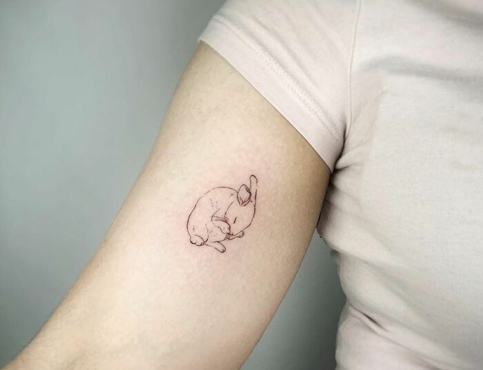 Minimal tattoo of a sleeping rabbit on an arm, showcasing delicate line work in understated tattoo design.