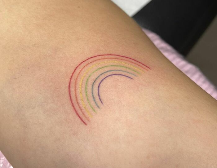 Minimal tattoo design of a colorful rainbow on skin.
