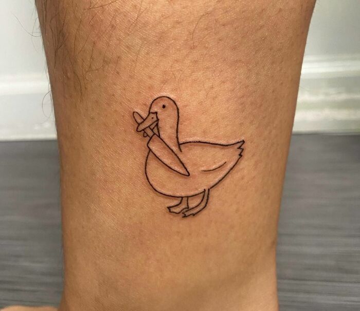 Minimal tattoo design of a duck holding a baguette on a person's skin.
