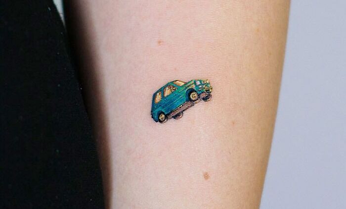 Minimal tattoo of a small, colorful car on a forearm.