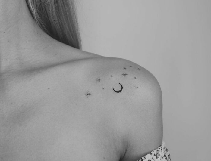Minimal tattoo design of stars and moon on a shoulder in black and white.