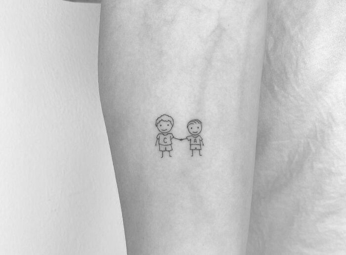 Minimal tattoo design of two stick figure characters holding hands on an arm.