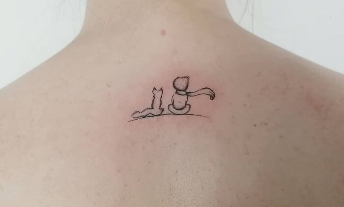 Minimal tattoo design of two cartoon cats sitting on a person's back, illustrating a simple yet elegant style.