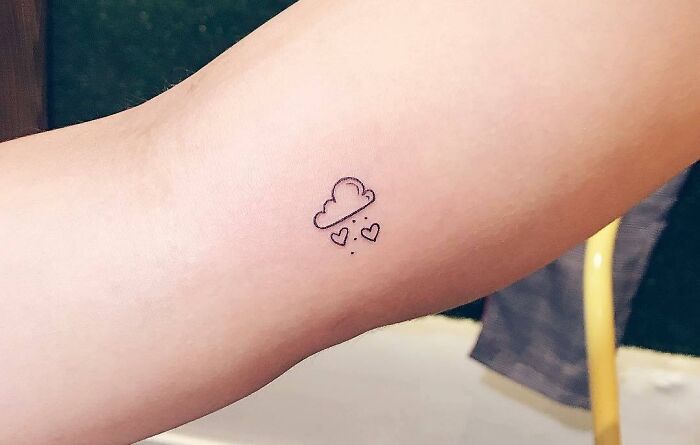 Minimal tattoo design of a small cloud with hearts on an arm.