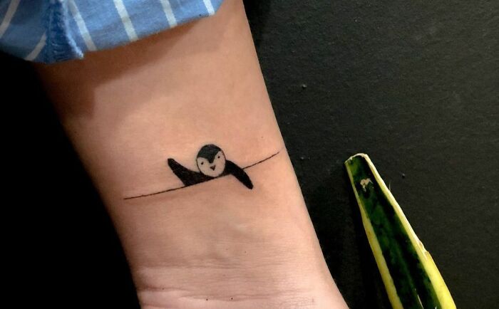 Minimal tattoo design featuring a small swimming penguin line art on an arm.