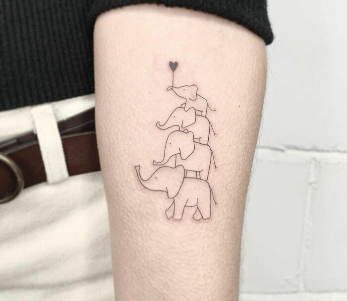 Minimal tattoo design of four outlined elephants with a heart balloon on the arm.