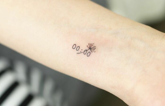 Minimal tattoo design of a delicate dandelion seed on an arm.