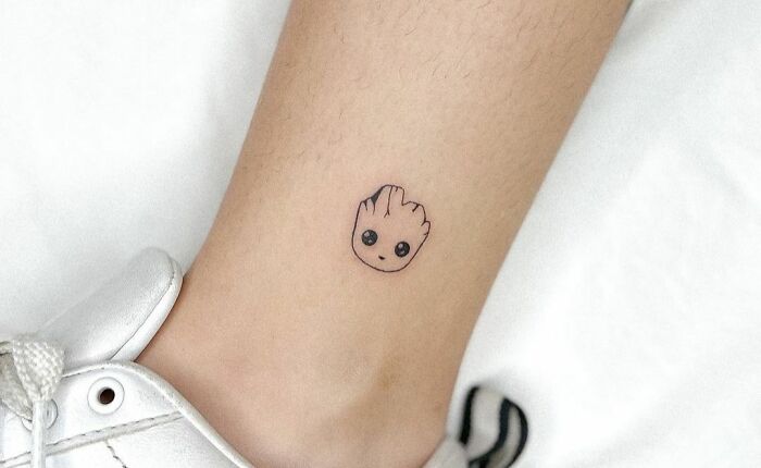 Minimal tattoo design of a cute small face on an ankle near a white shoe.