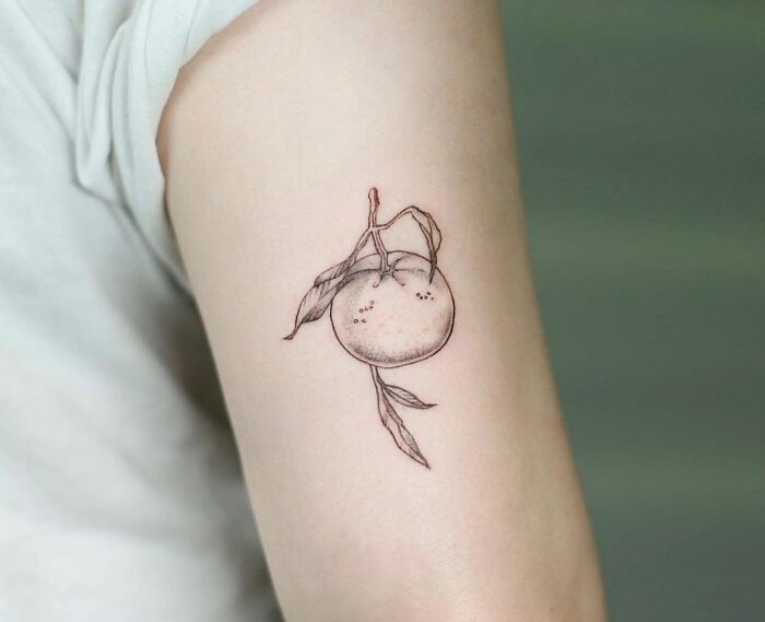 Minimal tattoo design of a delicate orange with leaves on an arm.