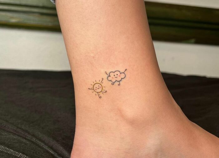 Minimal tattoo design of a smiling sun and cloud on an ankle.