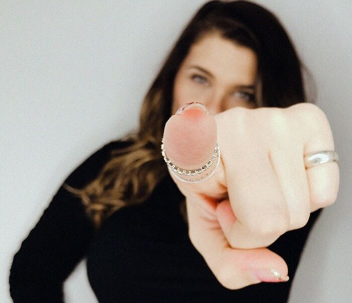 Young woman wearing rings pointing directly at the camera, illustrating engagement during texting games on phone conversations.