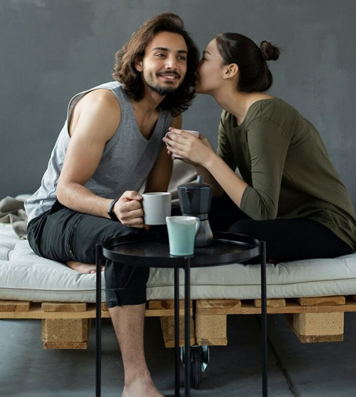 Couple enjoying coffee together while sitting on a couch, sharing a playful moment related to texting games.
