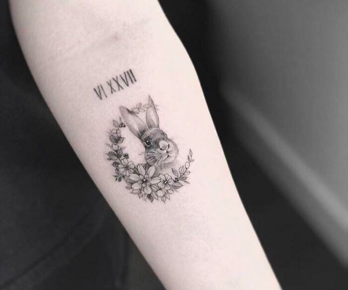 A rabbit tattoo enclosed in floral wreath with Roman numerals, capturing an adorable pet design.