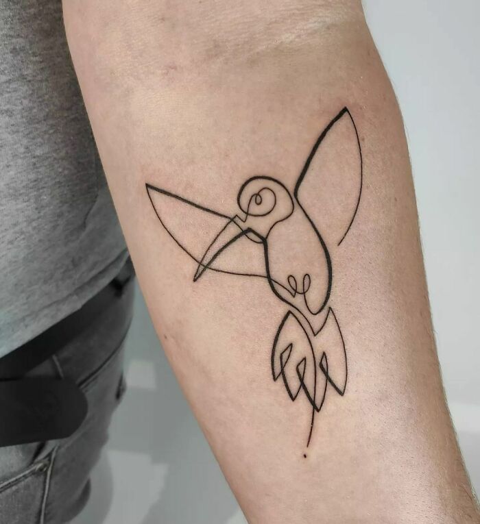 Single-line tattoo of a hummingbird on an arm, showcasing fine-line perfection.