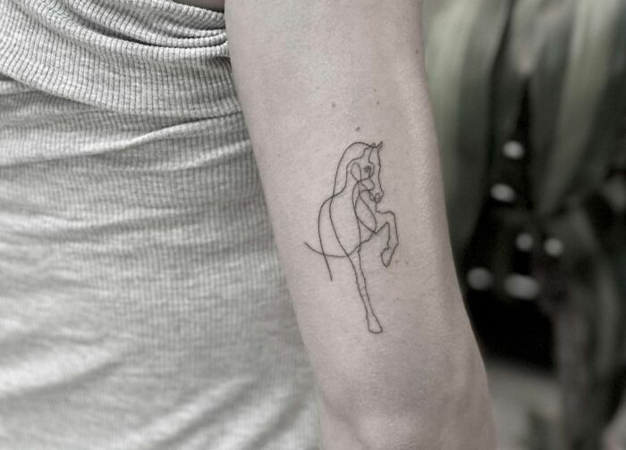 Single-line tattoo of a horse on an arm, showcasing fine-line perfection.