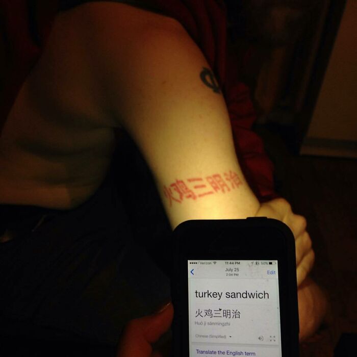 Funny tattoo of Chinese characters on an arm, humorously translated as "turkey sandwich" on a phone screen.