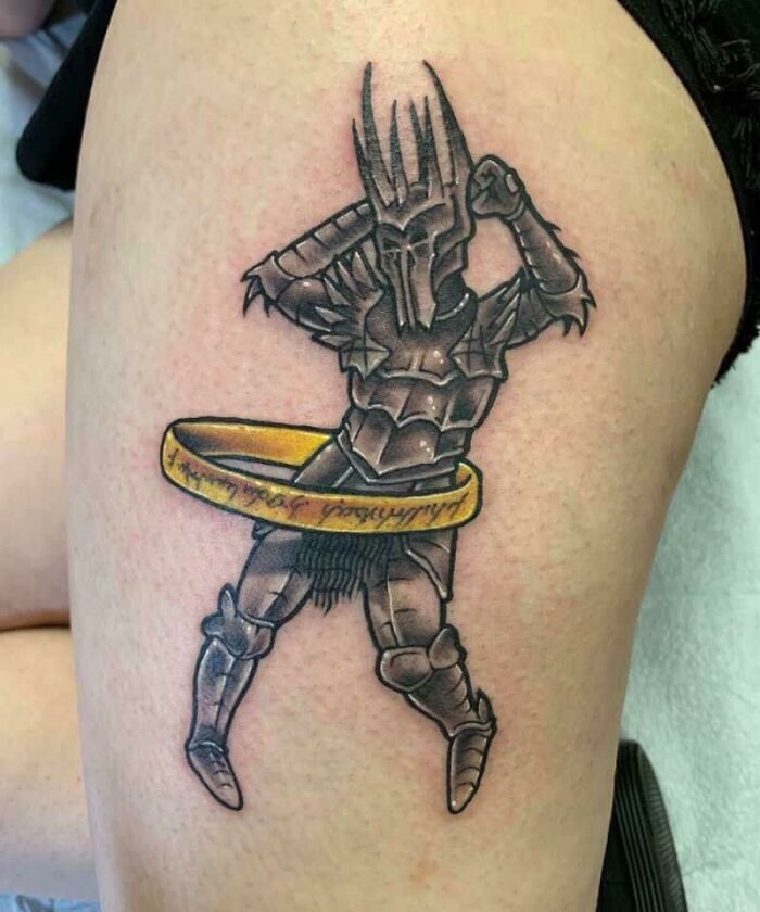 Funny tattoo of an armored figure hula hooping with a ring on the thigh.