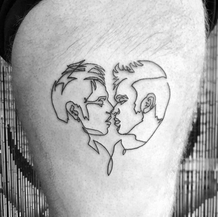 Fine-line tattoo of two faces in a single-line art style on a person's thigh.