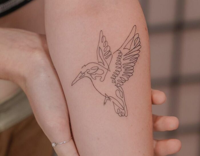 Fine-line single-line tattoo of a hummingbird on a person's arm, showcasing delicate artistry.
