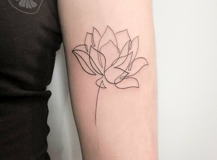 Single-line tattoo of a lotus flower on an arm, showcasing fine-line artistry.