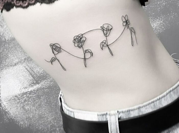 Fine-line tattoo of single-line flowers on a person's side.