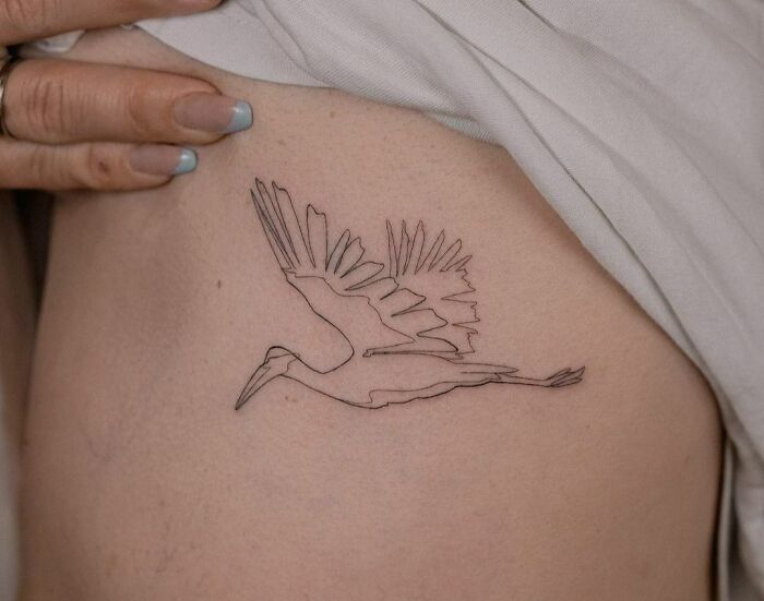 Fine-line single-line tattoo of a bird in flight on a person's side.