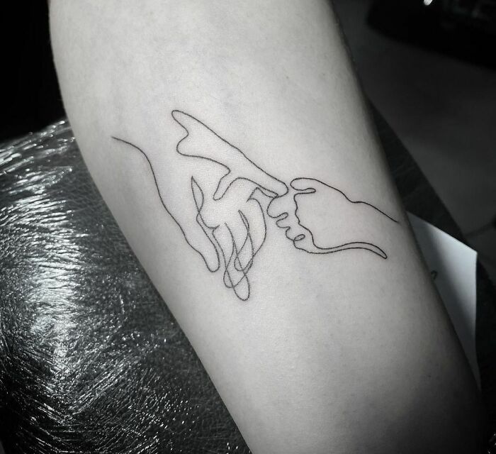 Fine-line single-line tattoo of two hands touching, on an arm.