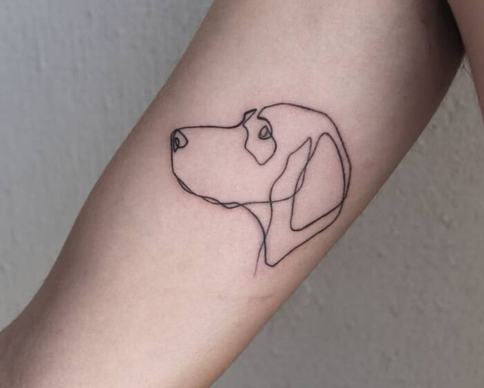 Single-line tattoo of a dog's face in fine-line style on an arm.