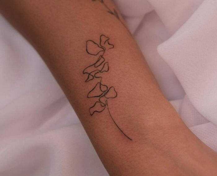 Fine-line tattoo of a floral design in single-line style on forearm.