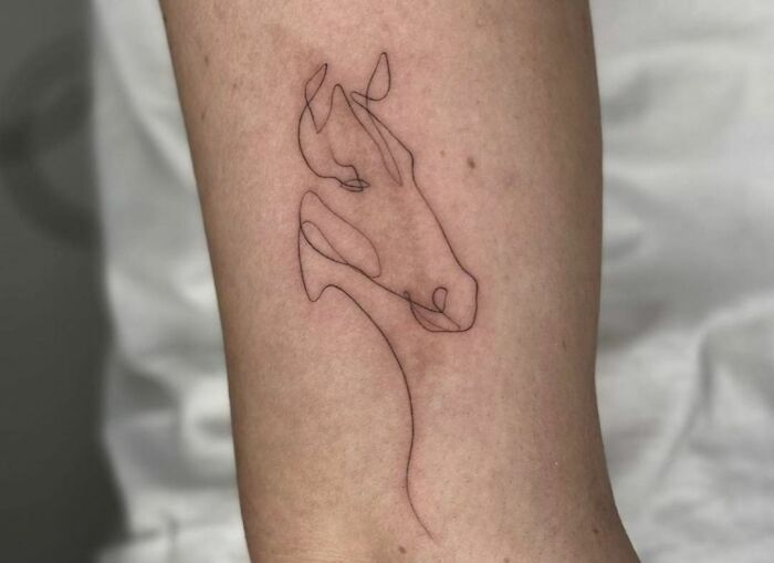 Fine-line single-line tattoo of a horse on forearm, showcasing minimalist artistry and delicate design.