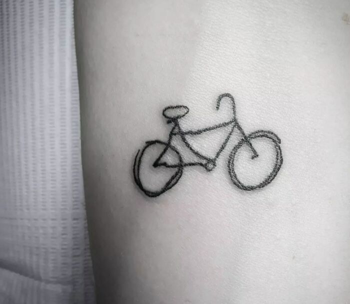 Single-line tattoo of a bicycle on skin, showcasing fine-line perfection.