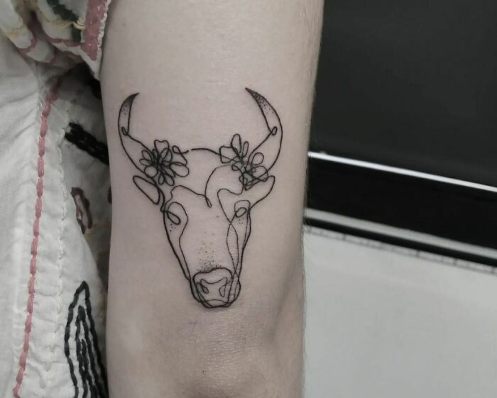 Single-line tattoo of a bull with floral details on an arm; showcases fine-line perfection.