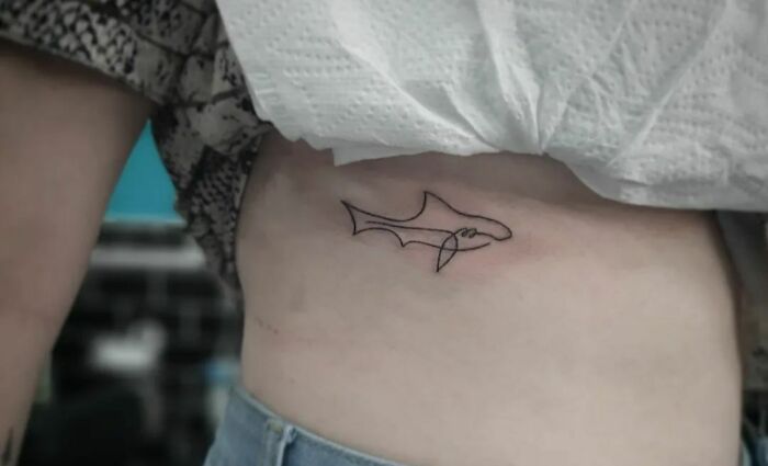 Single-line fine-line tattoo of a shark on a person's side, showcasing minimalist body art.