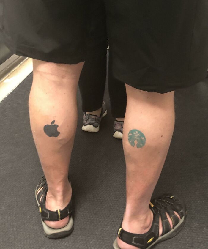 Funny tattoos on legs, featuring an Apple logo and a blue tree, seen on a person wearing sandals in a casual setting.