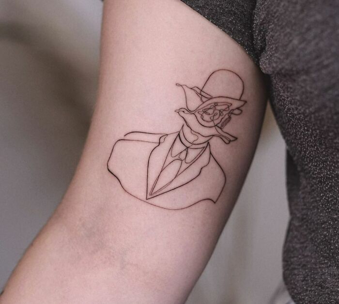 Fine-line single-line tattoo of a surreal face wearing a suit and hat on an arm.